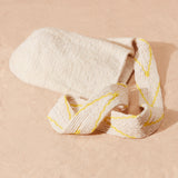 Flat view of ivory woven bag with yellow and beige v patterned strap on a sand surface