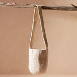 Ivory woven crossbody bag with ivory and yellow V pattern strap hanging on a branch against a biege background
