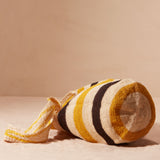 Bottom view of striped woven bag with yellow, black, and beige colors on a sand background