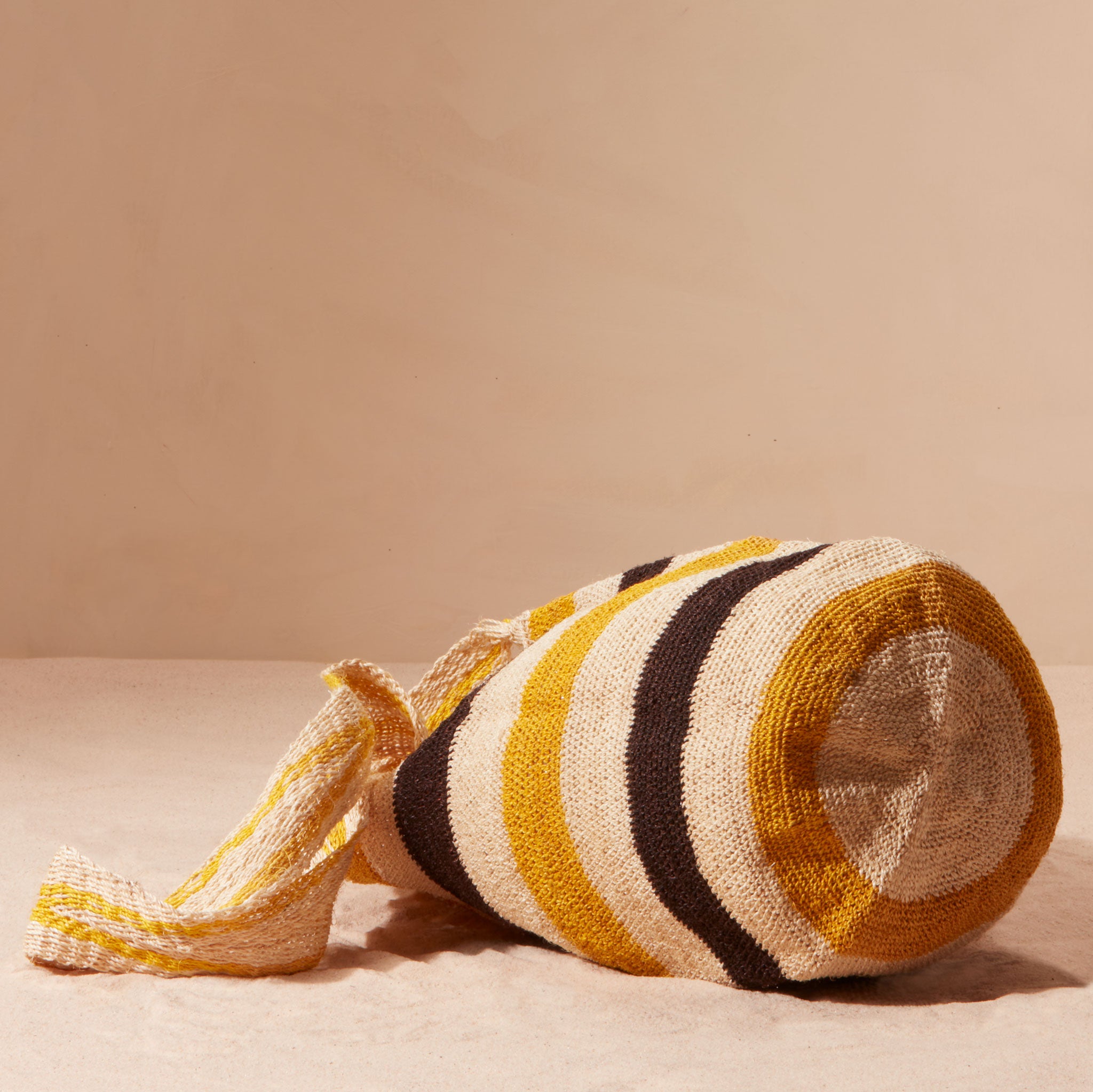 Bottom view of striped woven bag with yellow, black, and beige colors on a sand background