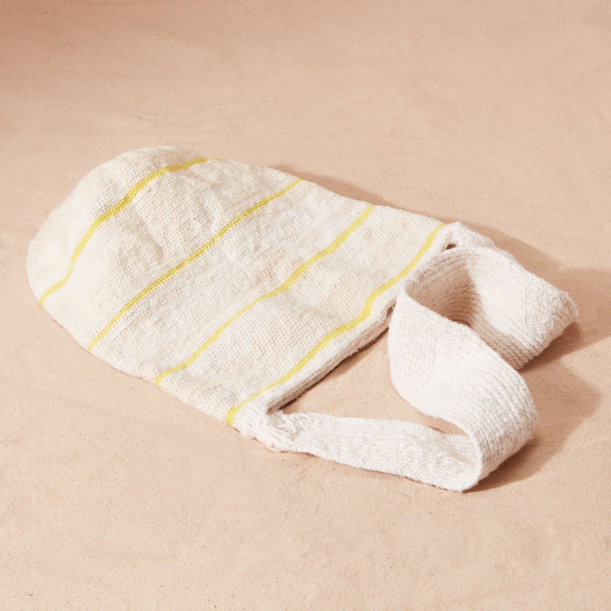 Ivory woven bag flat view with thin yellow stripes and a solid woven strap on a sand background
