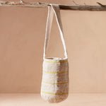 Woven bag with thin yellow stripes hanging from a branch against a beige background