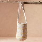 Woven bag with thin yellow stripes hanging from a branch against a beige background