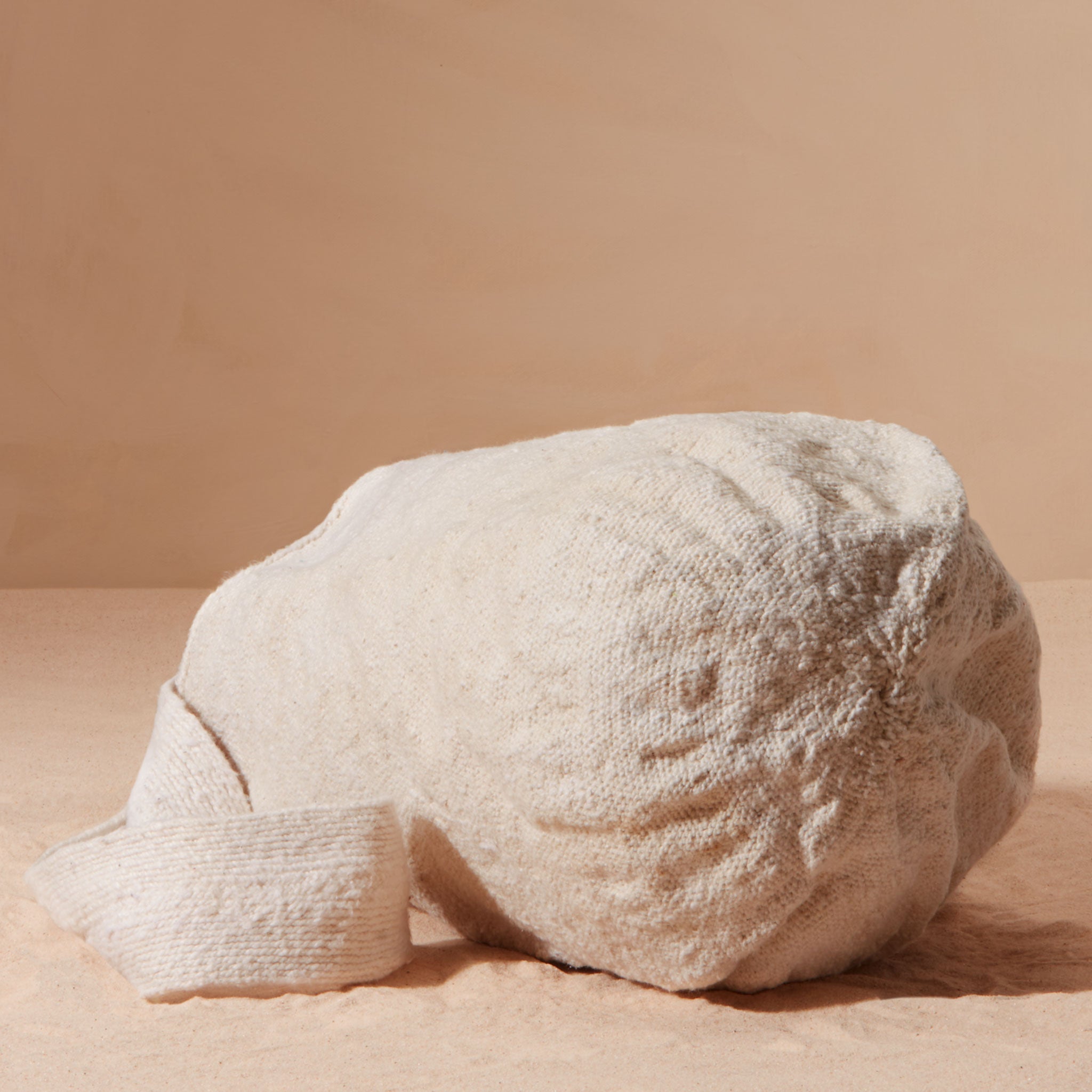 Bottom view of woven ivory bag against a beige background