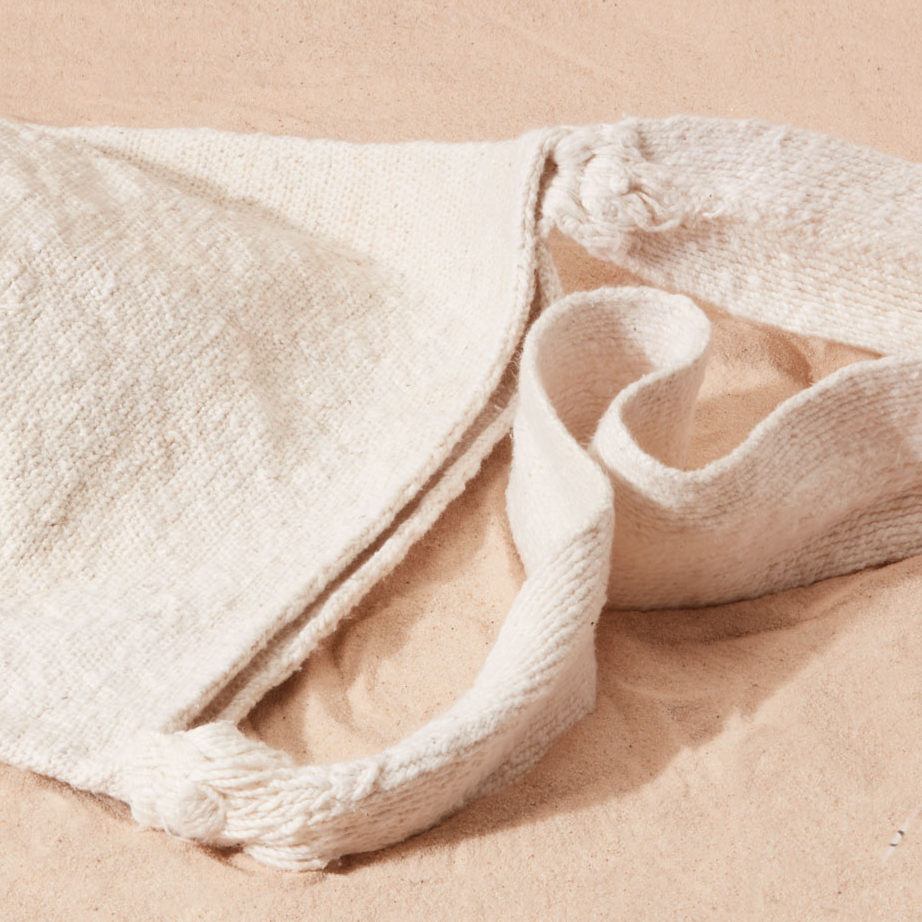 Detail view of strap of ivory woven bag on a sand surface