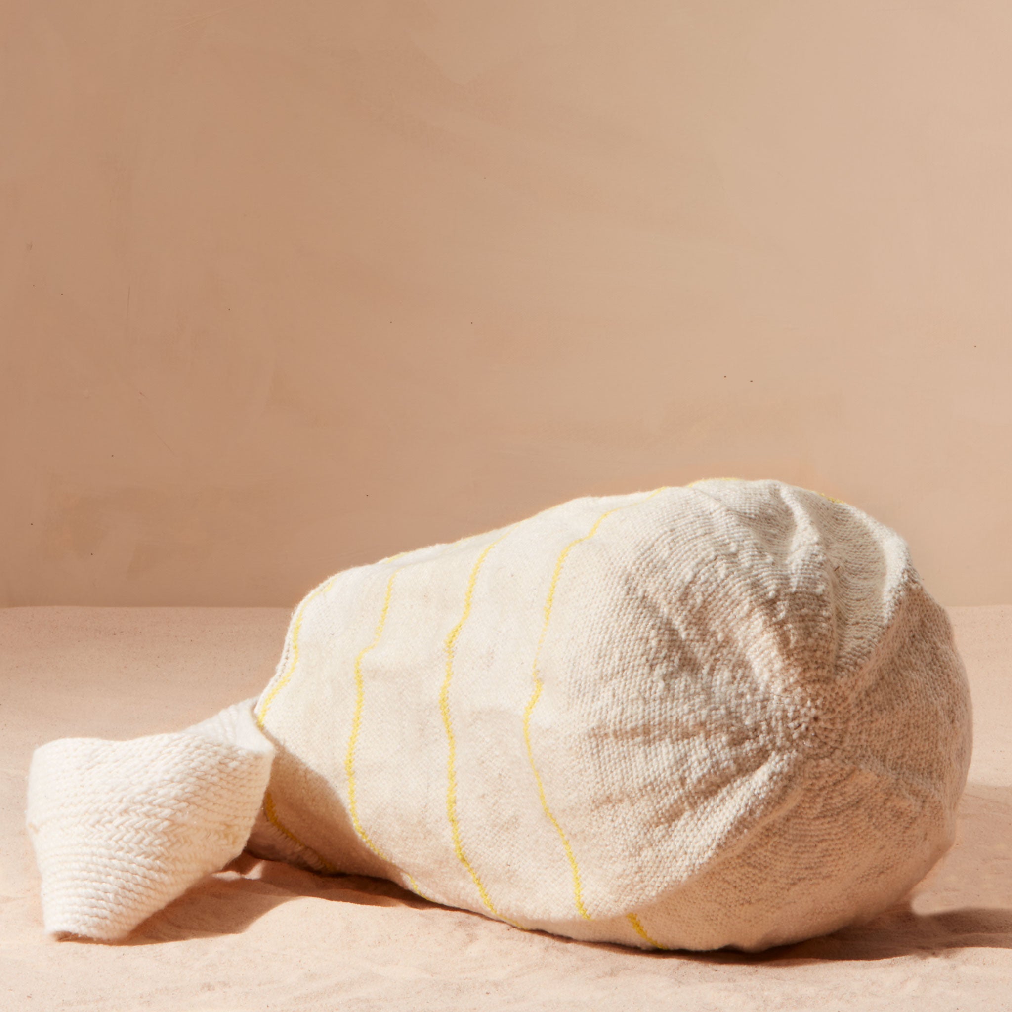 Bottom view of ivory woven bag with thin yellow stripes on a beige background