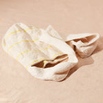 Flat view of ivory woven bag with thin yellow stripes on a sand background