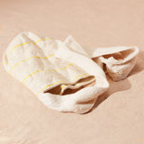 Flat view of ivory woven bag with thin yellow stripes on a sand background