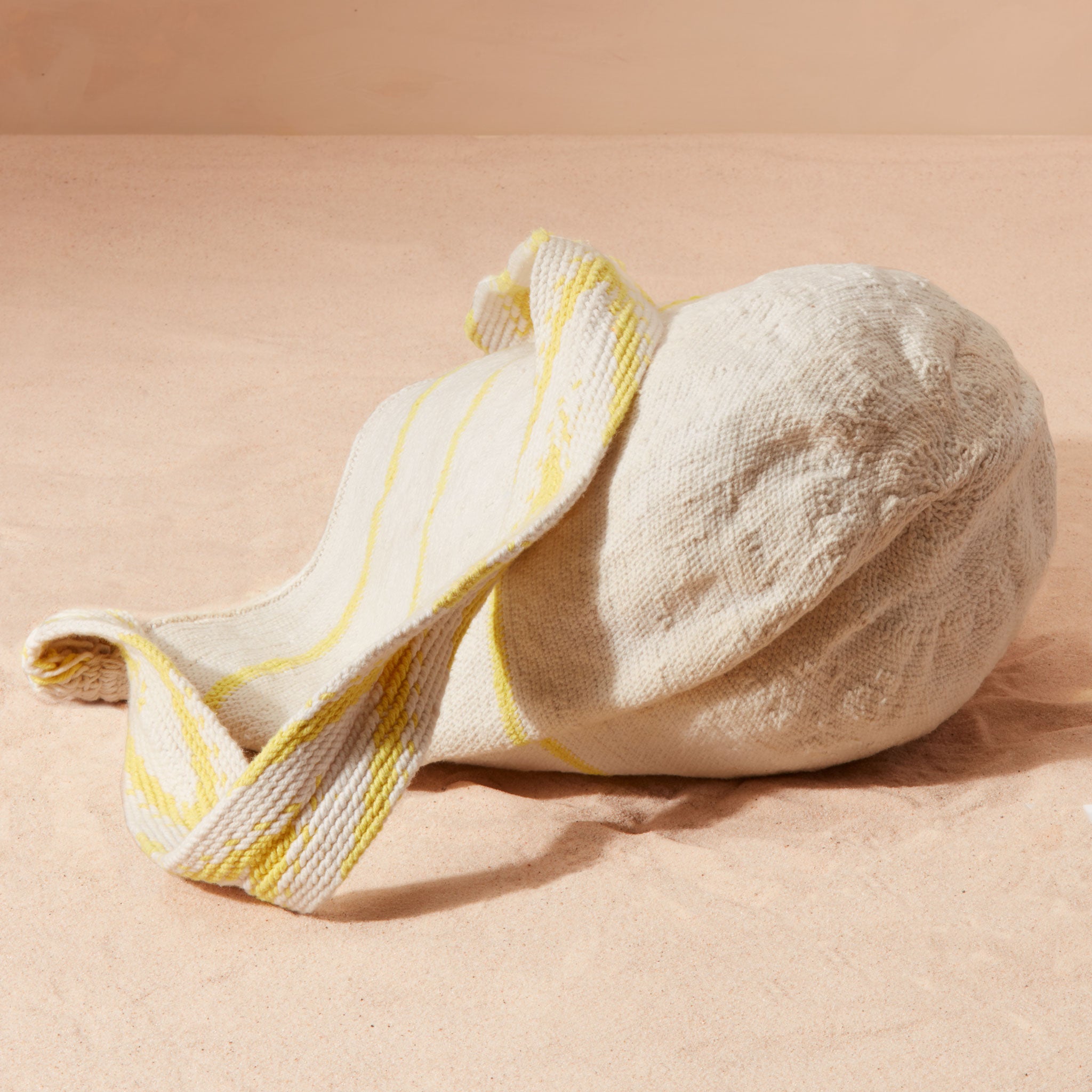 Bottom view of ivory and yellow woven striped bag with V patterned yellow and ivory strap on a beige background