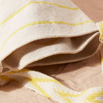 Detail view of ivory woven bag with thin yellow stripes and yellow V patterned bag showing the bag has two compartments against a sand background