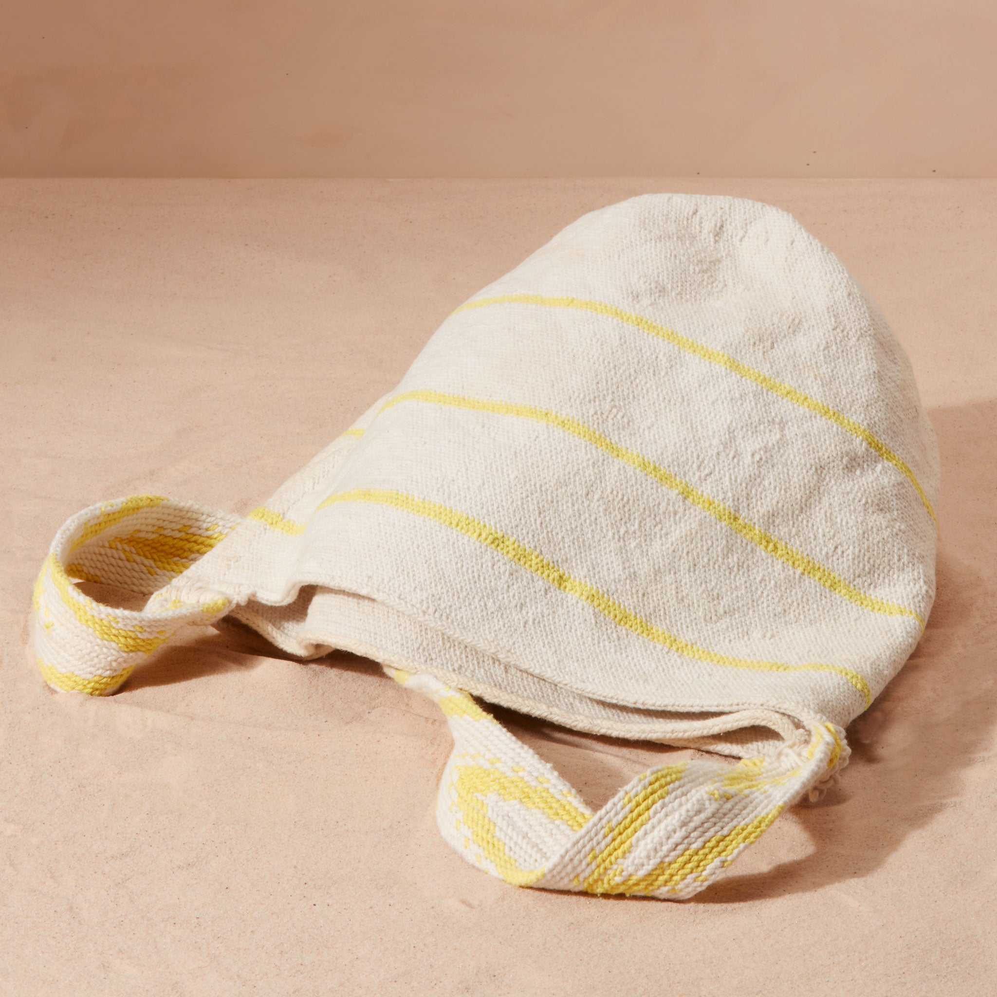 Flat view of ivory and yellow striped woven bag on a sand background