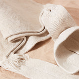 Detail view of lose weave of strap of an ivory woven bag on a sand surface