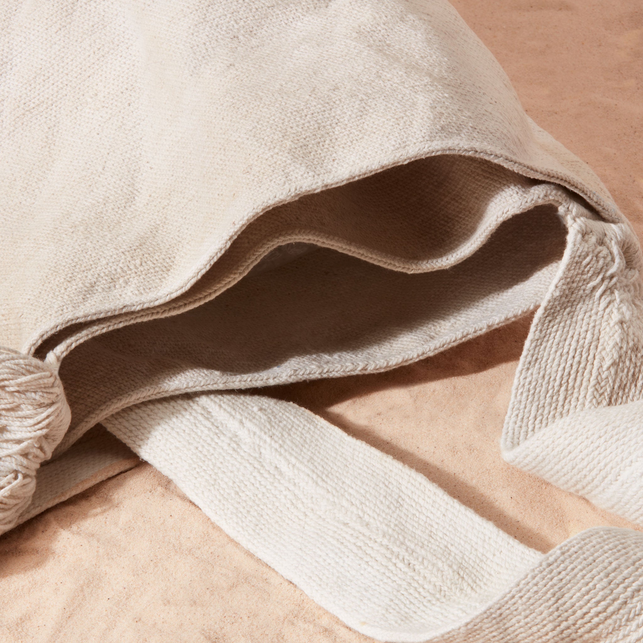 Detail view of ivory woven bag showing two interior compartments of the bag on a sand surface