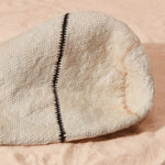 Detail view of slightly stained bottom of ivory woven bag with beige and black stripes on a sand surface