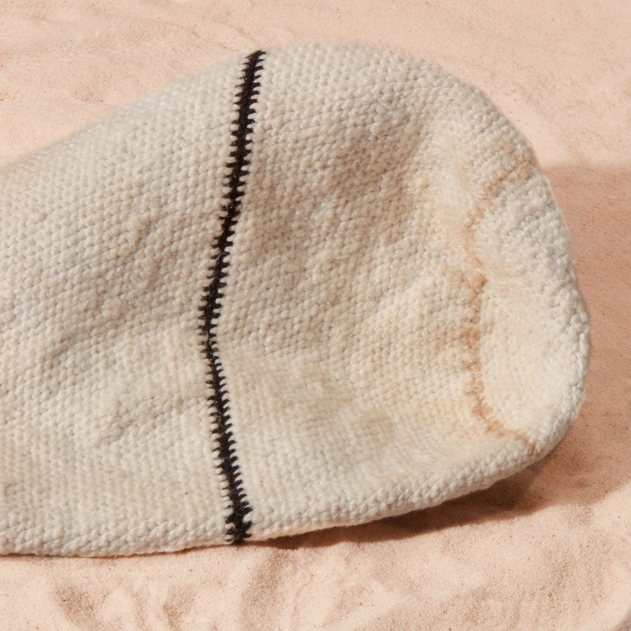 Detail view of slightly stained bottom of ivory woven bag with beige and black stripes on a sand surface