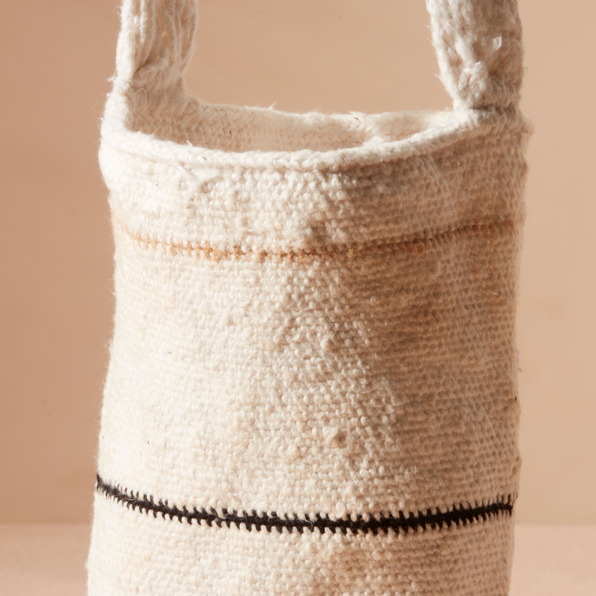 Detail view of lose weave of straps of and ivory woven bag with yellow/brown and black thin stripes