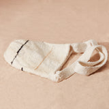 Flat view of ivory woven bag with black and yellow/brown and black thin stripes on a sand surface
