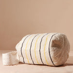 Bottom view of ivory woven bag with thin black and yellow stripes against a beige background