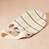 Flat view of ivory woven bag with thin black and yellow stripes against a sand background