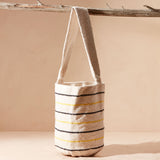Ivory woven bag with black and yellow stripes with a strap hanging from a branch against a beige background
