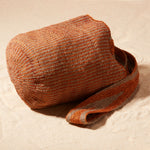 Side View of Brown-orange and grey woven bag with a strap on a sand background