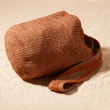 Side View of Brown-orange and grey woven bag with a strap on a sand background