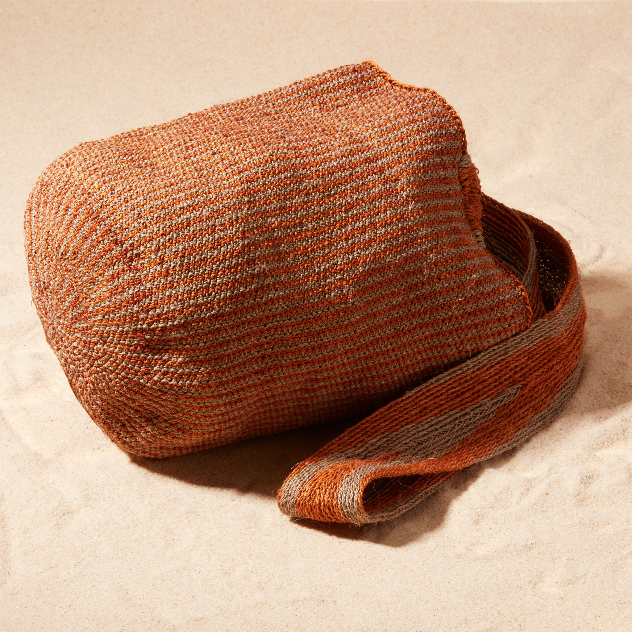 Side View of Brown-orange and grey woven bag with a strap on a sand background