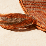 Close up view of Brown-orange and grey woven bag with strap on a sand background