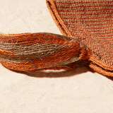 Close up view of Brown-orange and grey woven bag with strap on a sand background