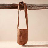 Woven brown-orange and grey bag with a strap hanging on a branch against a beige background
