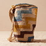 Hand-woven bag with brown, yellow, blue, ivory geometric pattern against a beige background