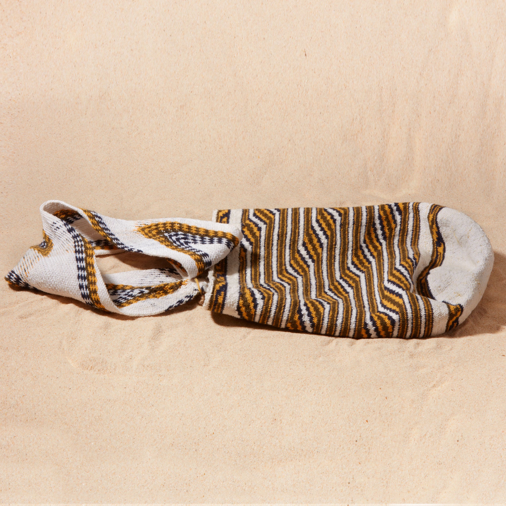 Flat view of ivory, black and yellow woven bag on a sand surface