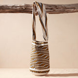 Ivory, black and yellow woven bag hanging on a wooden branch against a beige background