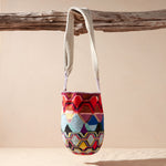Colorful patterned woven bag hanging from a branch on a beige background