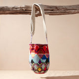 Colorful patterned woven bag hanging from a branch on a beige background