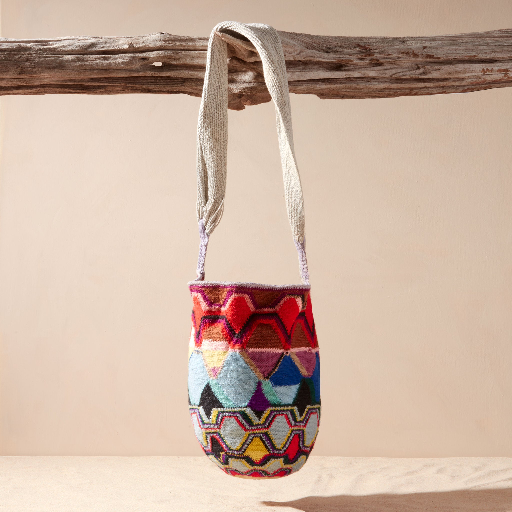 Colorful patterned woven bag hanging from a branch on a beige background