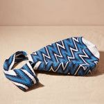 Flat view of woven bag with blue and white zigzag pattern on a sand surface