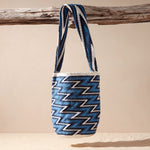 Woven bag with blue and white zigzag pattern hanging on a branch against a beige background