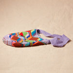 Flat view of colorful geometric-patterned bag with a purple strap on a sand surface