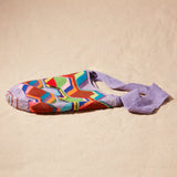 Flat view of colorful geometric-patterned bag with a purple strap on a sand surface
