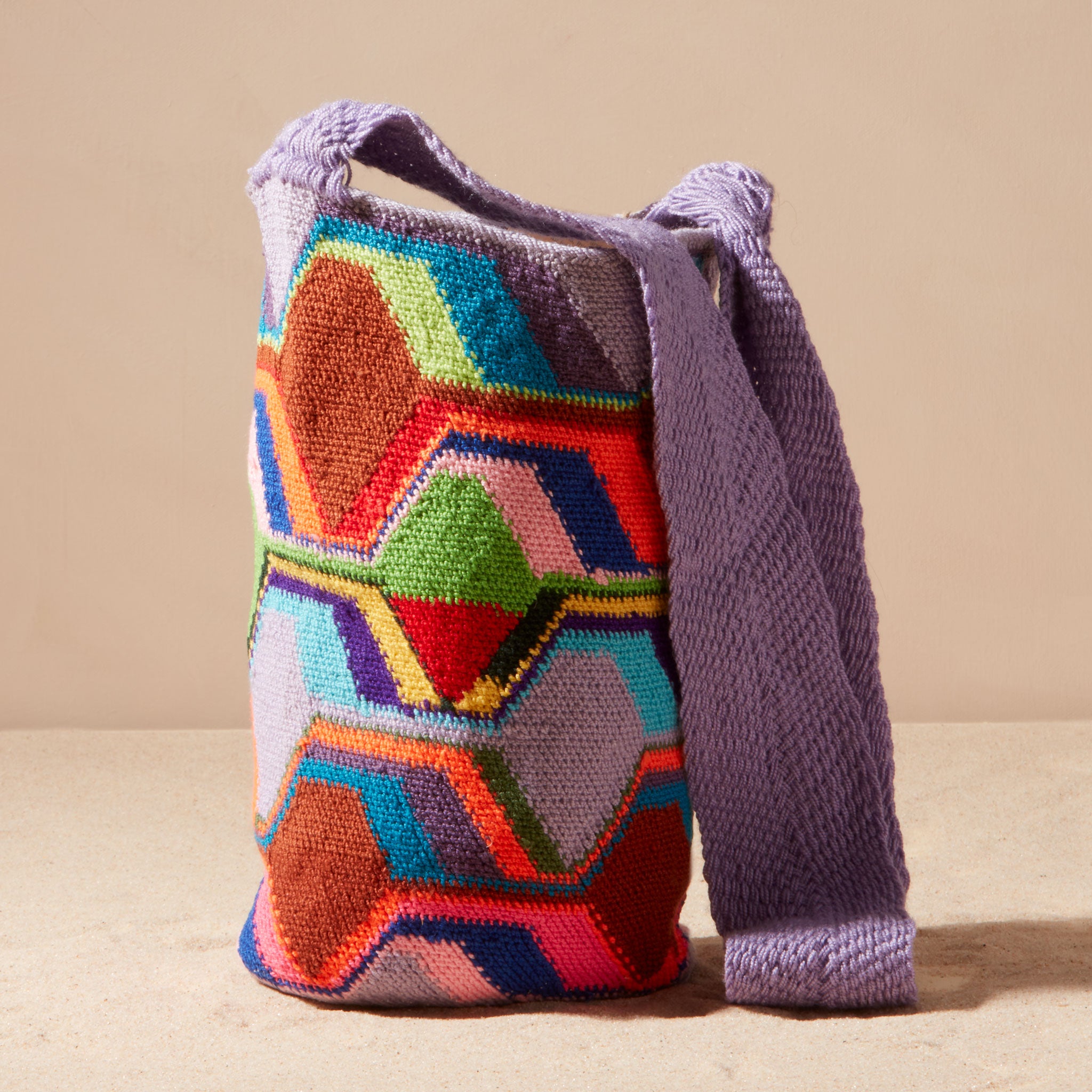 Colorful geometric-patterned bag with a purple strap against a beige background