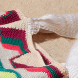 Close-up of white woven strap of colorful bag with geometric pattern on a sand background
