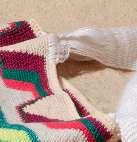 Close-up of white woven strap of colorful bag with geometric pattern on a sand background