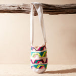 Colorful patterned woven bag hanging on a wooden branch against a beige background