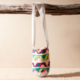 Colorful patterned woven bag hanging on a wooden branch against a beige background