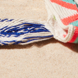 Close-up of a colorful woven bag with blue, white, strap on a sand surface
