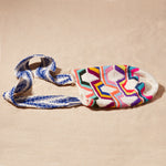 Flat view of colorful woven bag with a blue and ivory strap on a beige background