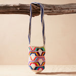 Colorful woven bag with geometric pattern hanging on a wooden branch against a beige background