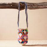 Colorful woven bag with geometric pattern hanging on a wooden branch against a beige background