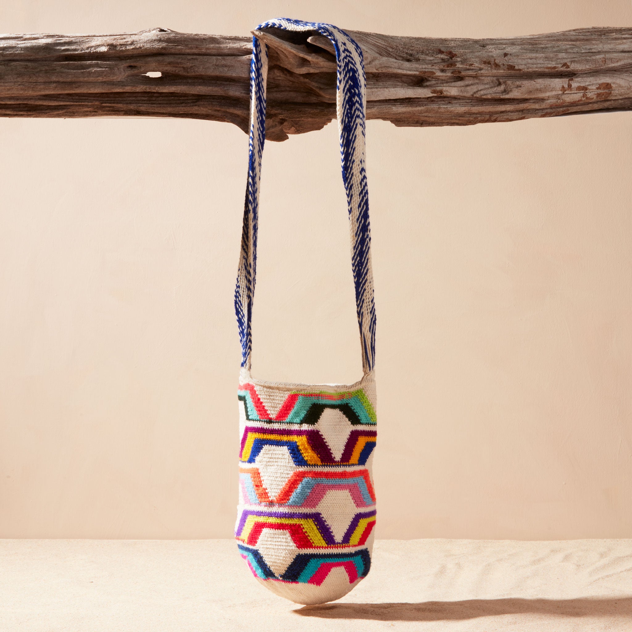 Colorful woven bag with geometric pattern hanging on a wooden branch against a beige background